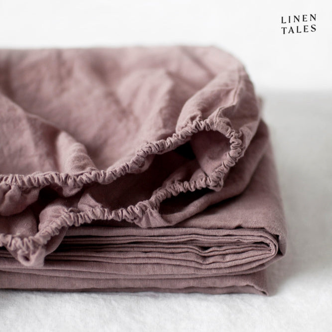 A muted blush fitted sheet in sustainably sourced, certified 100% pure linen beautifully folded, breathable, and irresistibly soft.