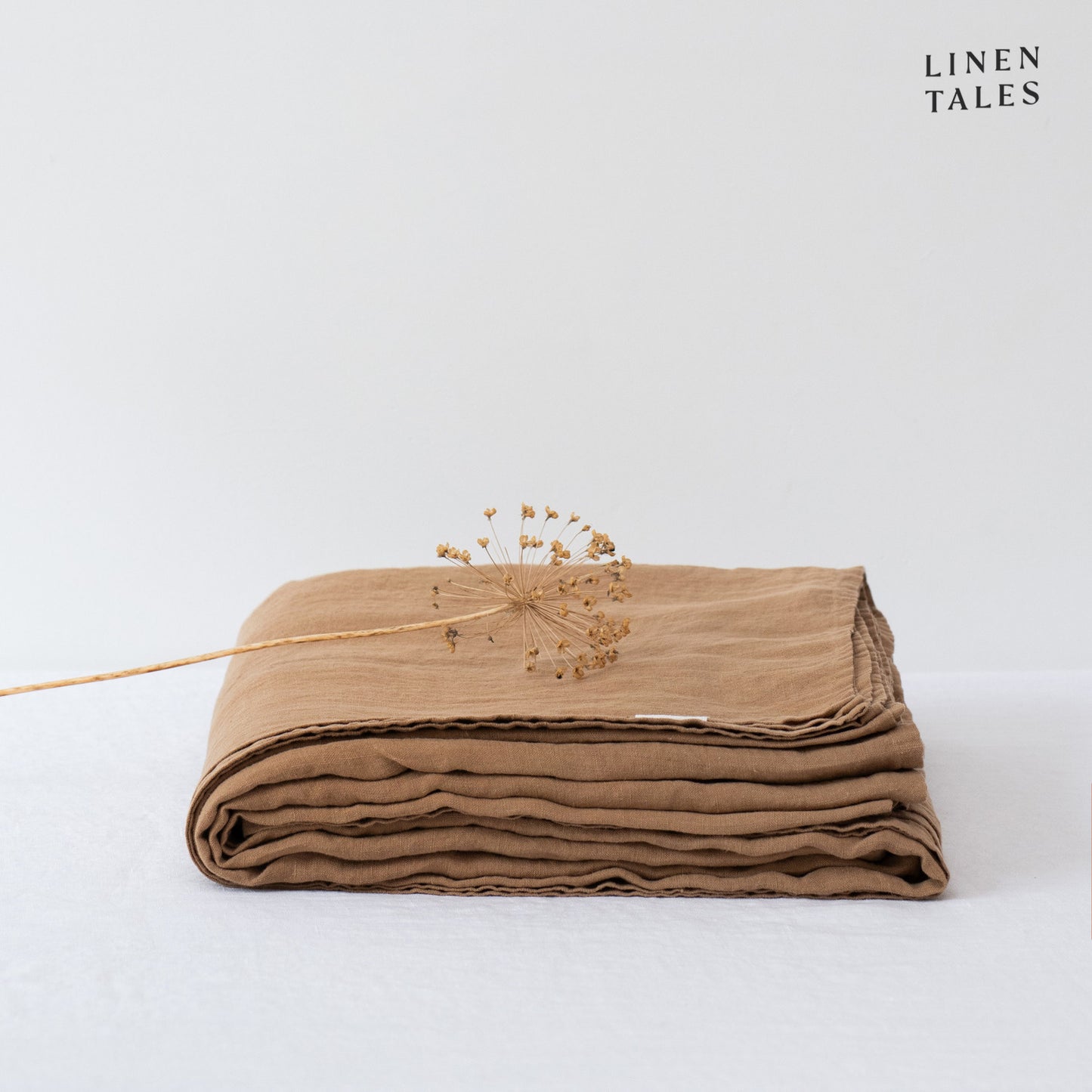 A folded fitted 100% pure linen flat sheet in warm camel, exuding a rich, earthy elegance.