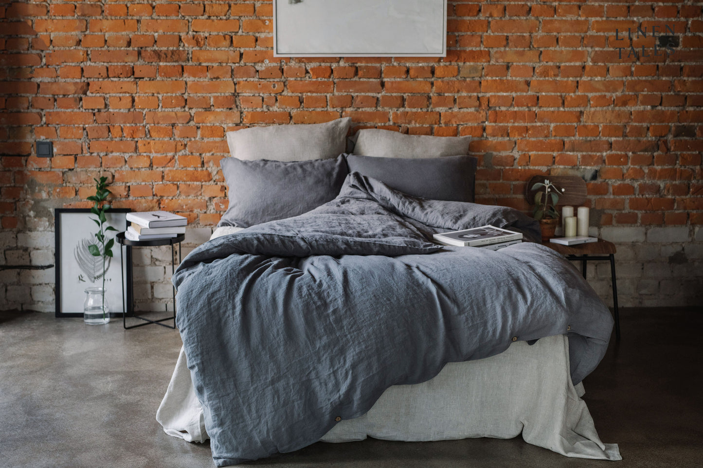 A beautifully made linen bed set against a rustic brick wall, framed by elegant side tables, timeless charm meets natural comfort.