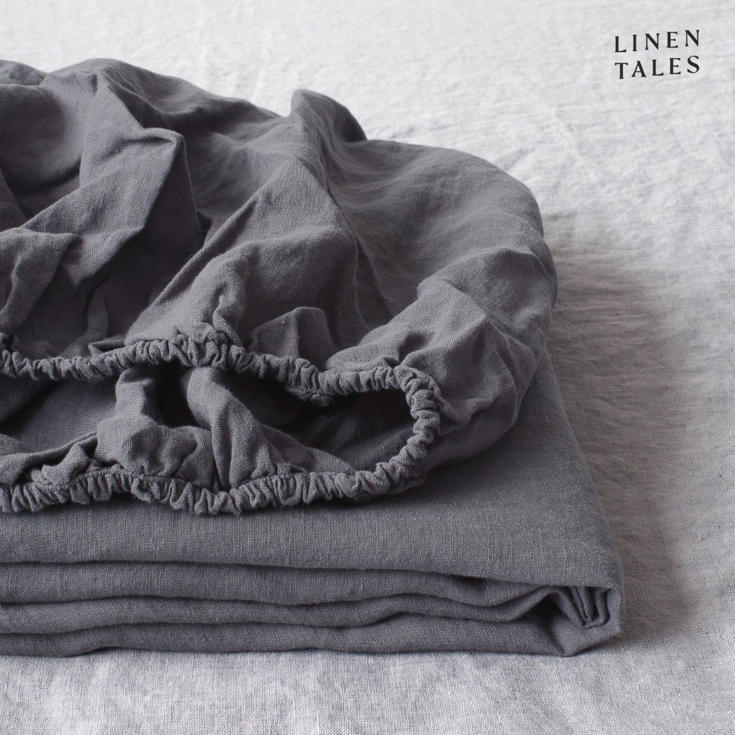 A rich dark grey fitted sheet, expertly folded to showcase its certified 100% pure linen—sustainably sourced, moisture-wicking, and naturally soft.