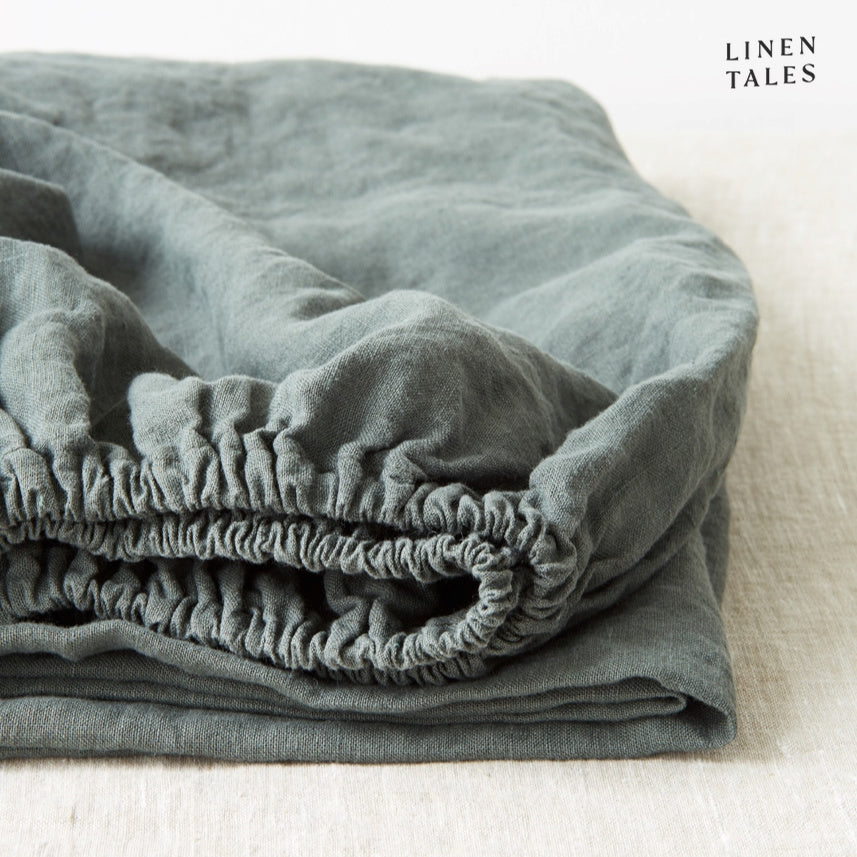 A deep forest green fitted sheet in certified 100% pure linen, folded to showcase its eco-friendly, thermoregulating properties for restful sleep.