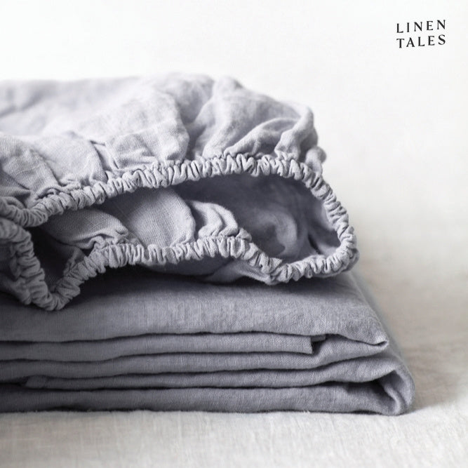 A soft light grey fitted sheet in certified 100% pure linen, neatly folded to reveal its stone-washed texture sustainable, breathable, and refined