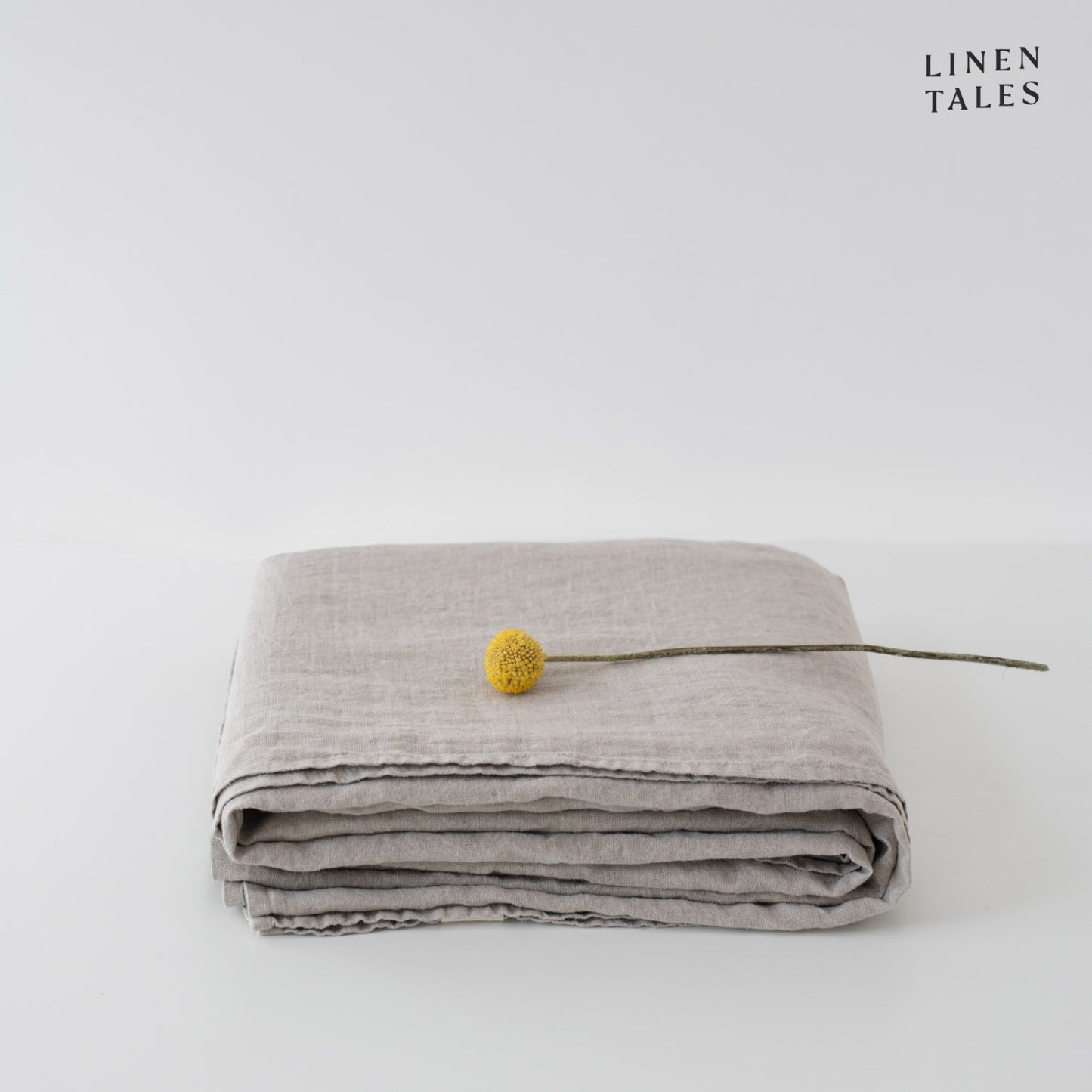 A folded fitted 100% pure linen flat sheet in soft natural flax, revealing its organic beauty and timeless appeal.