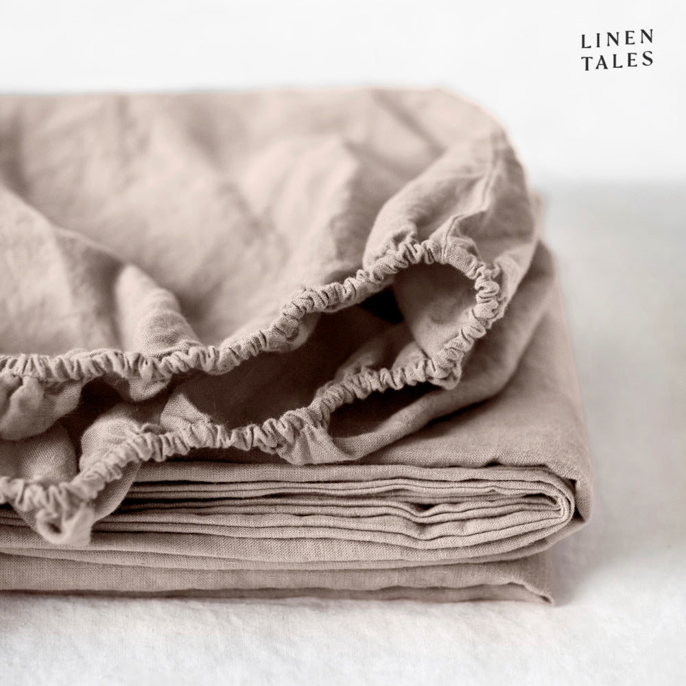 A rich taupe linen fitted sheet, folded with elegance, crafted from certified 100% pure linen ethically sourced, stone-washed, and naturally breathable.