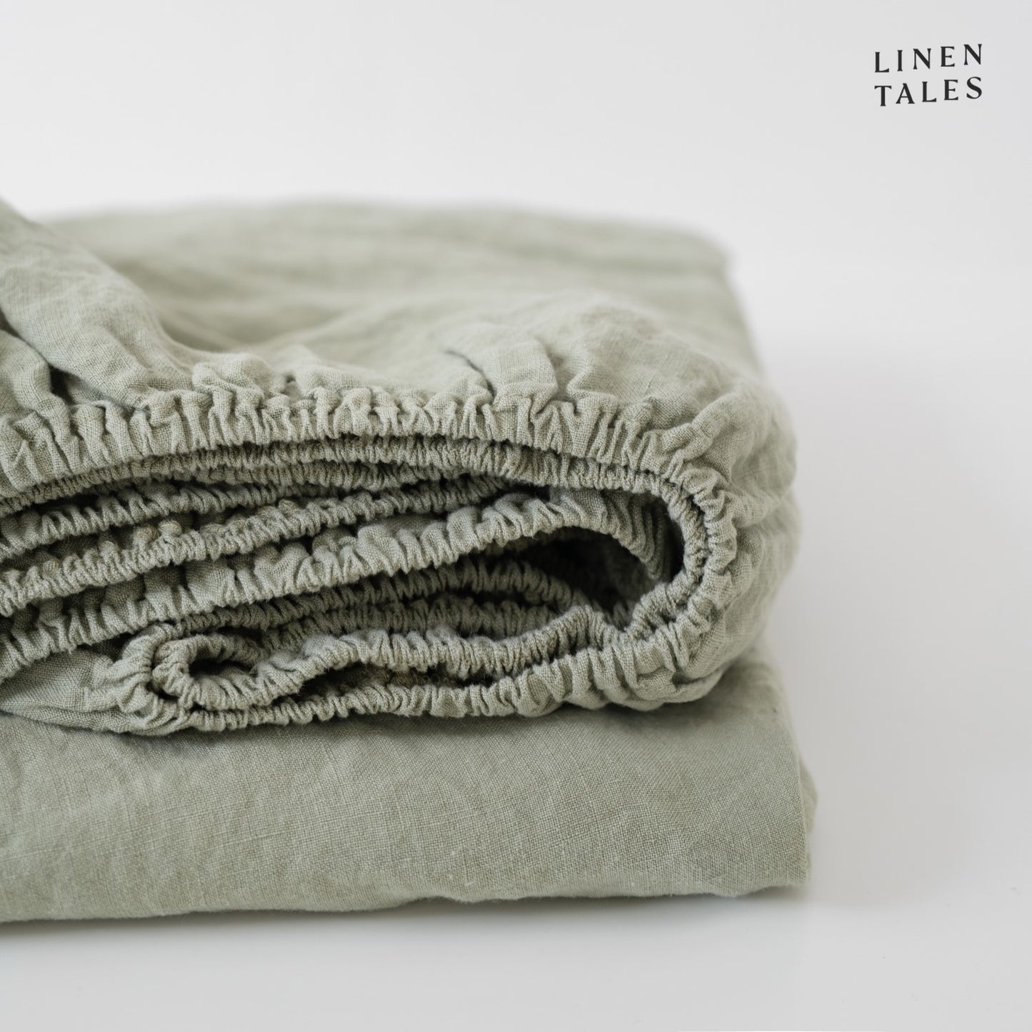 A muted sage green linen fitted sheet, folded to highlight its sustainable, certified 100% pure linen soft, breathable, and naturally calming