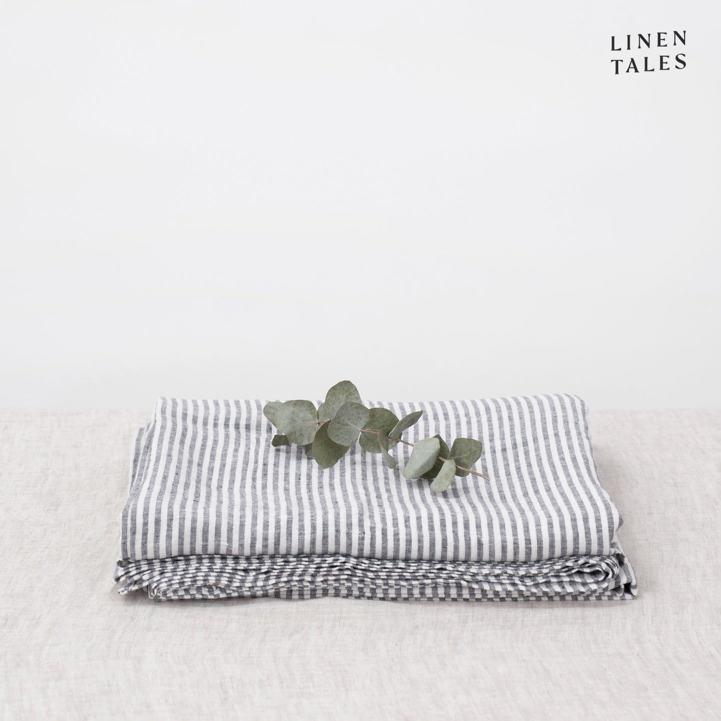 A folded fitted 100% pure linen flat sheet with thin black stripes, adding subtle contrast and refined detail.