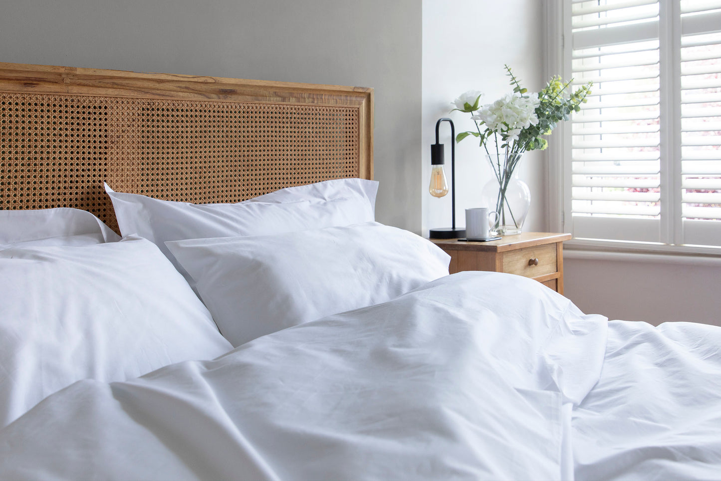 Bed with white 100% Organic Cotton bedding set including duvet cover, standard and oxford pillowcases, and wooden headboard in a bright bedroom.