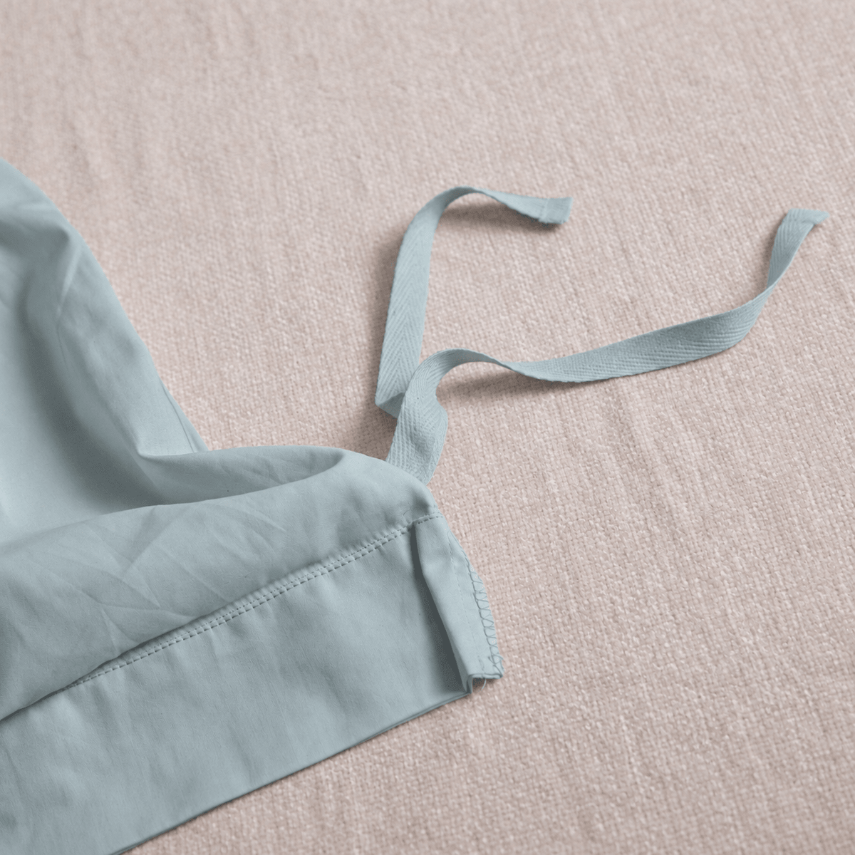 A close-up of a light sage green fabric strap or trim with a matching fabric piece laid on a textured beige surface.