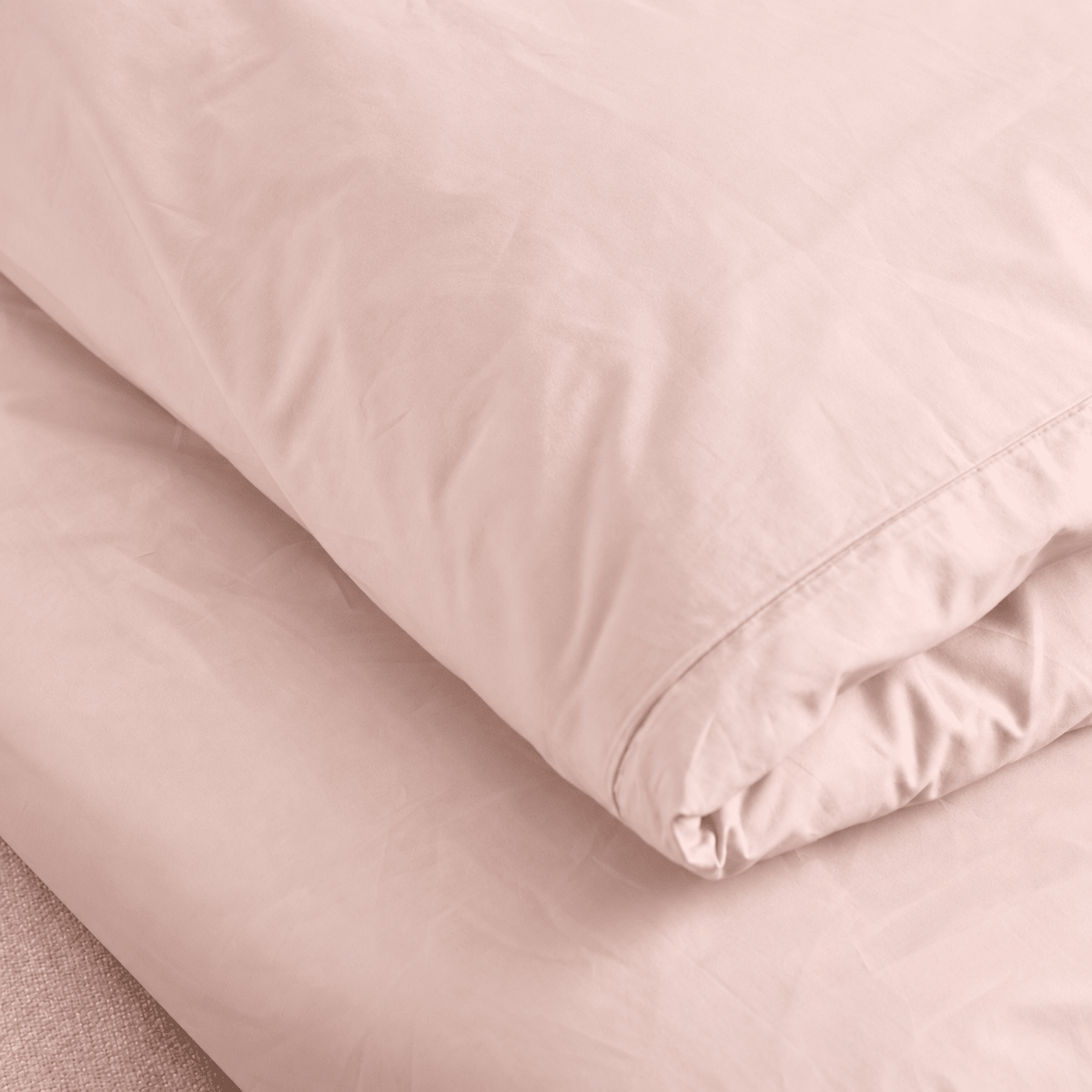 A close-up of a folded dusty pink bedding set, showing the smooth texture of the duvet cover and matching fitted sheet.