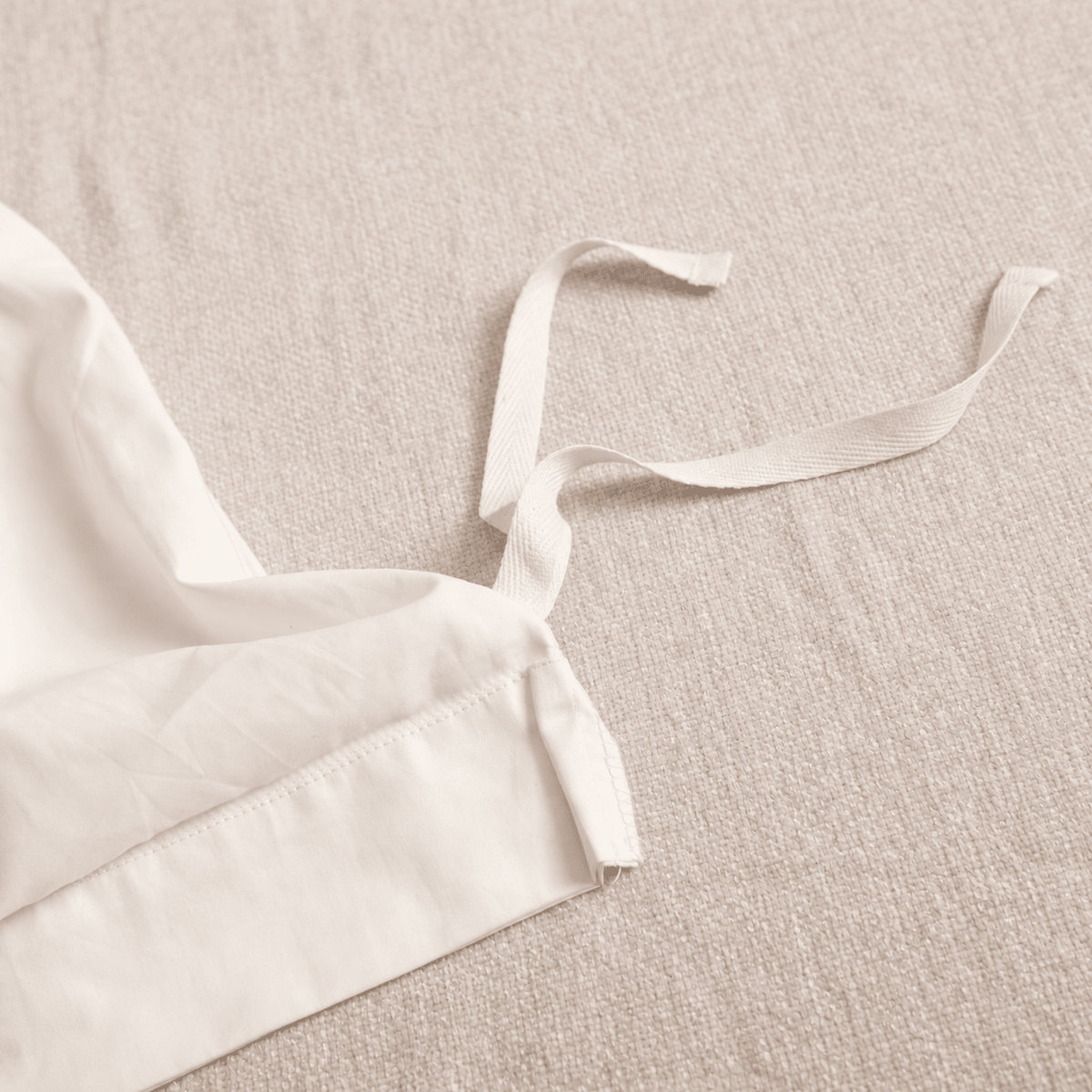 Close-up of a white fabric garment with a tie strap laid on a textured beige fabric background.
