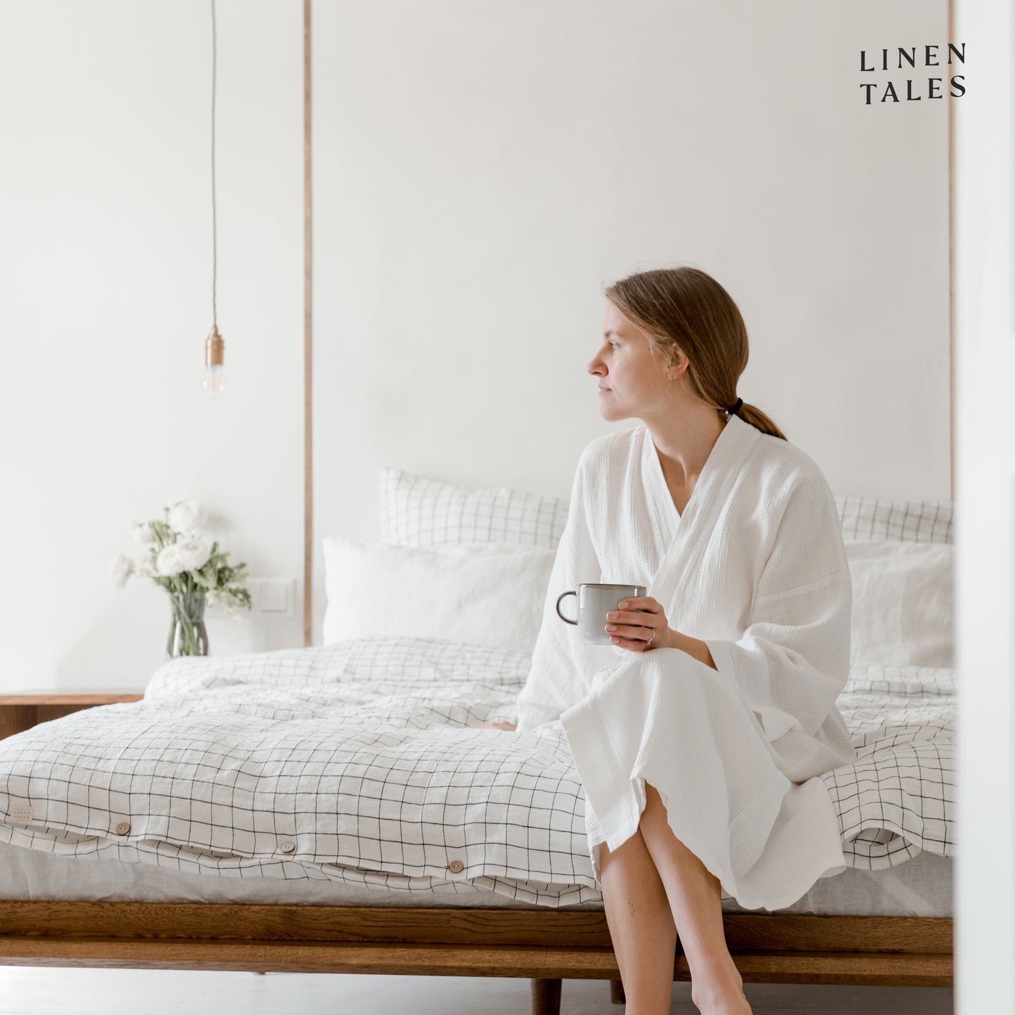 A woman sits gracefully on the bed, effortlessly smoothing a white linen duvet cover into place an elegant touch to a perfectly made bed.