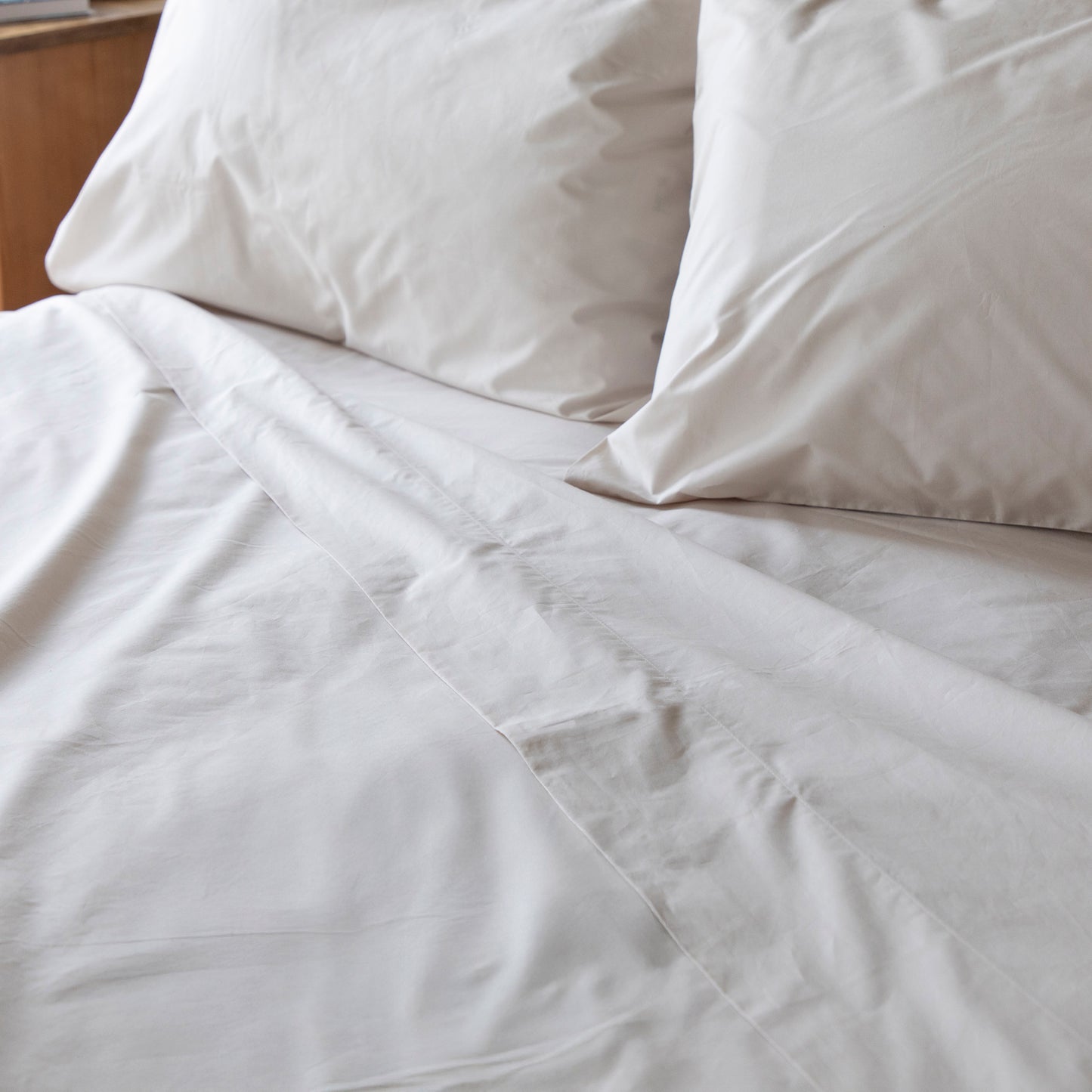 Close-up of folded back flat sheet in driftwood natural pure 100% organic cotton bedding with pillows on a bed.
