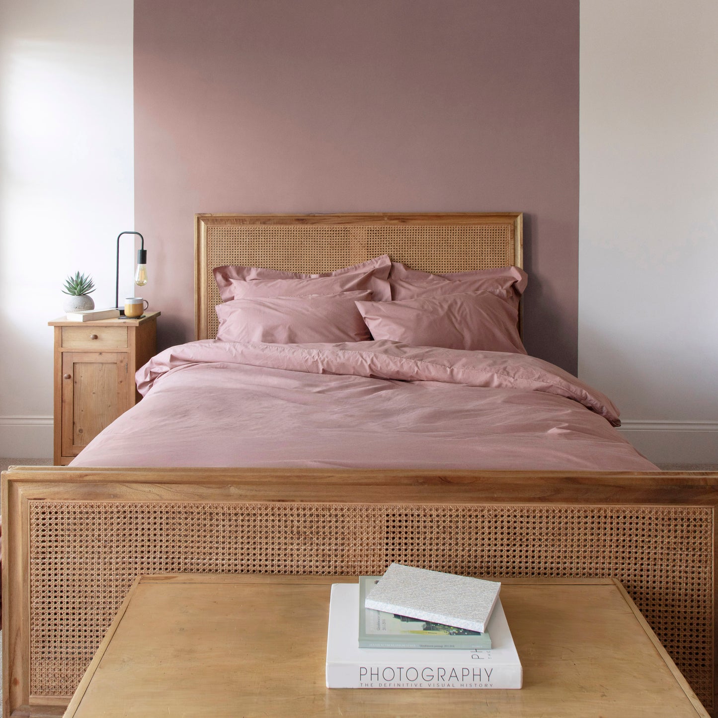 Bedroom with wooden bed frame, dune shadow clay coloured 100% organic cotton bedding, including duvet cover, pillow cases and fitted bed sheets and a side table.