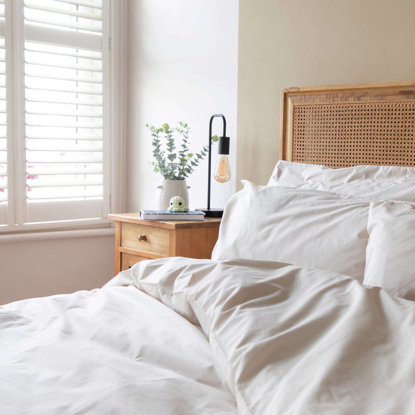 Neatly made bed with driftwood, neutral 100% Organic Cotton bedding in a bright bedroom.