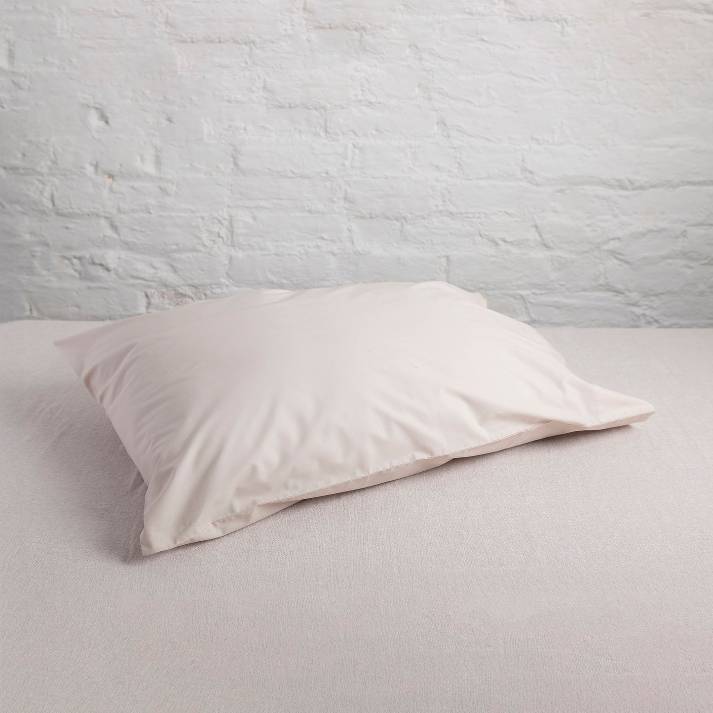 Driftwood colour natural cotton pillowcase on a light gray bed against a white brick wall.