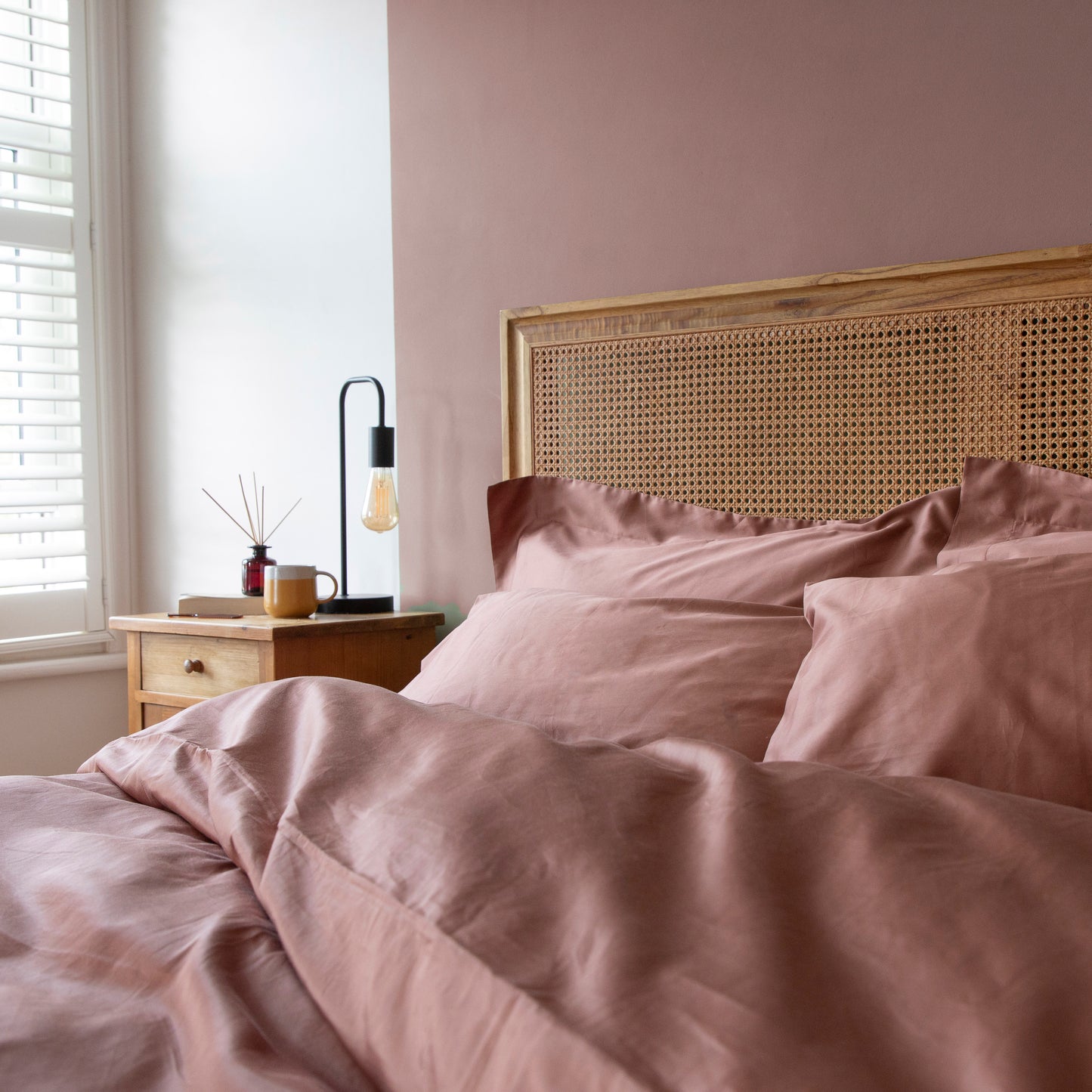 Cross bedroom shot with dune shadow clay coloured 100% organic cotton bedding, including duvet cover, pillow cases and fitted bed sheets and a wicker headboard.