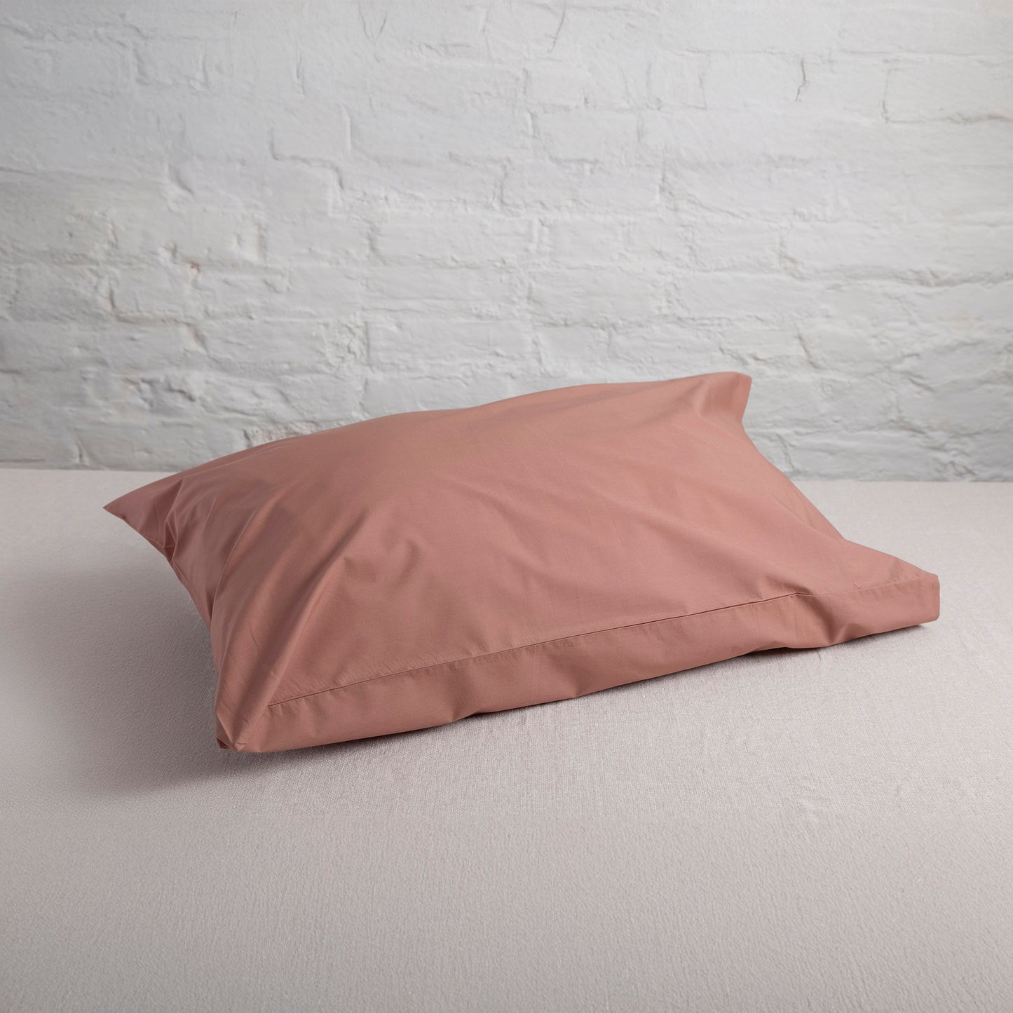 Dune Shadow organic cotton pillowcases on a light gray surface with a white brick wall background