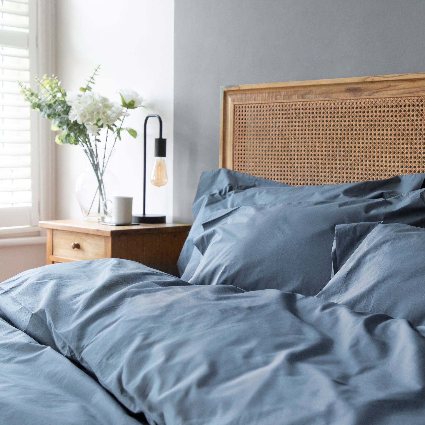 Bed with Linen Bay Sargasso blue 100% organic cotton bedding and wooden headboard in a bedroom setting.