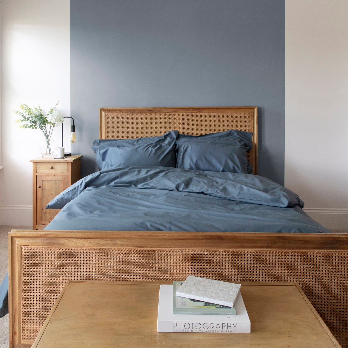 Bedroom with wooden bed frame, Linen Bay Sargasso blue 100% organic cotton bedding, and a side table.