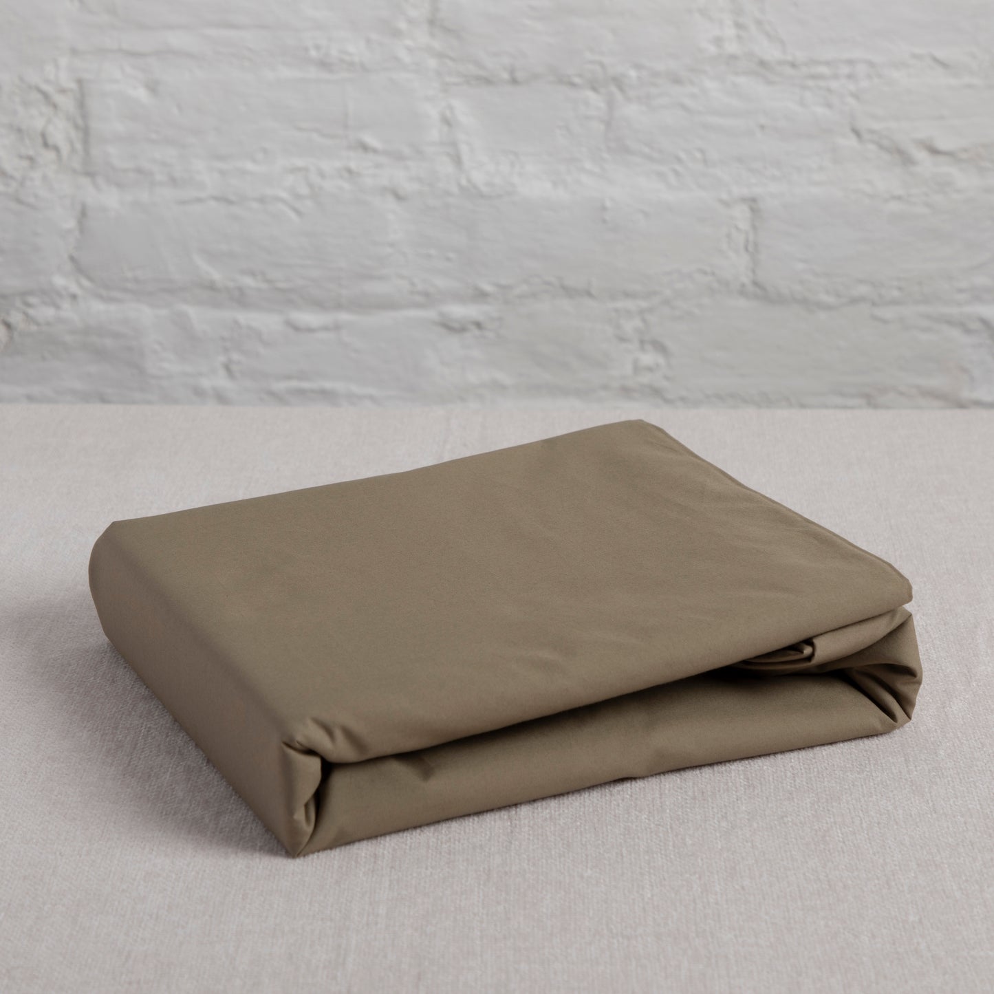 Folded sea fern 100% organic pure cotton  flat sheet on a light gray surface with a textured gray wall background
