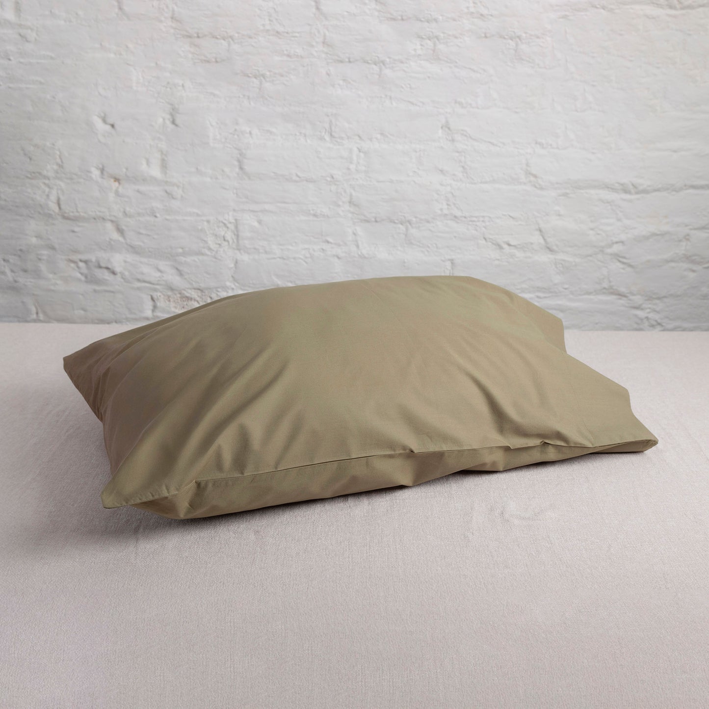 Seafern, dark green pillow on a light grey cotton surface against a white brick wall.