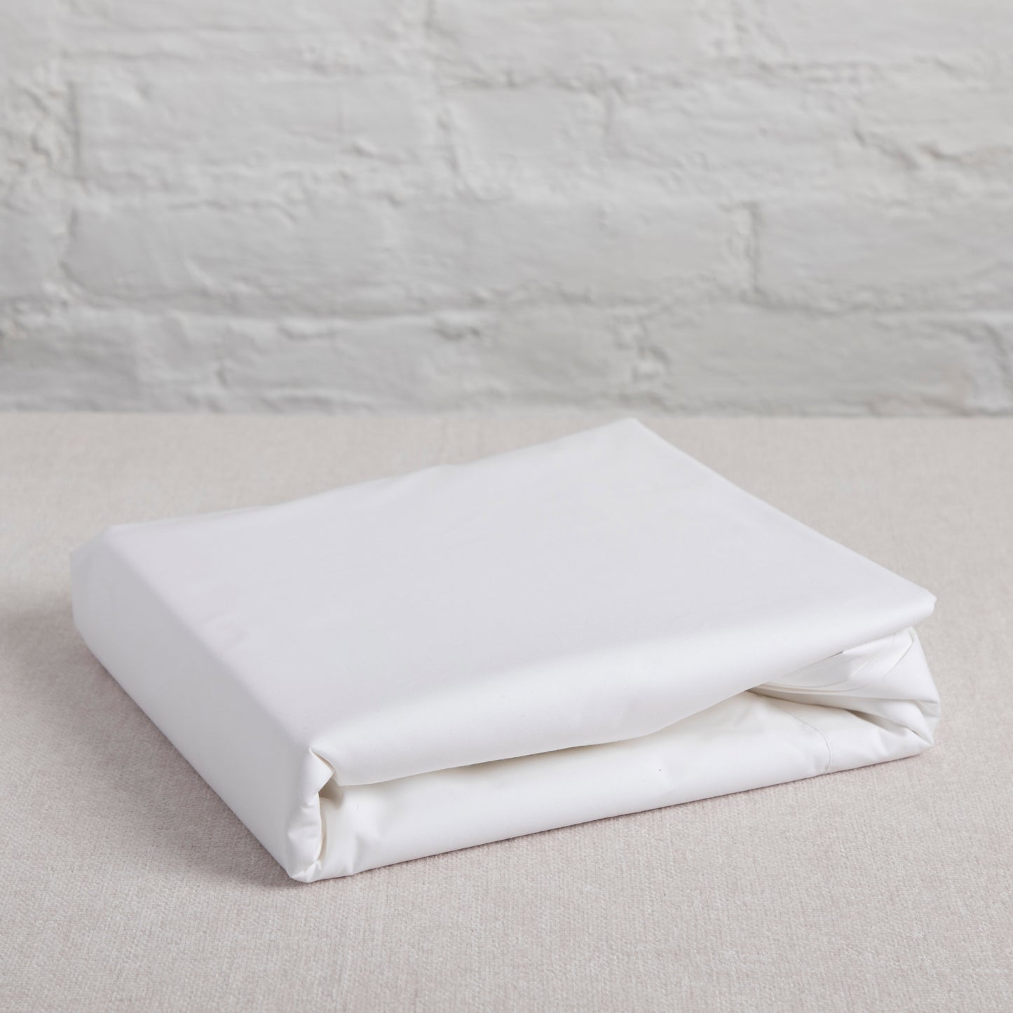 Folded sea salt white fitted sheet on a light gray surface with a neutral background