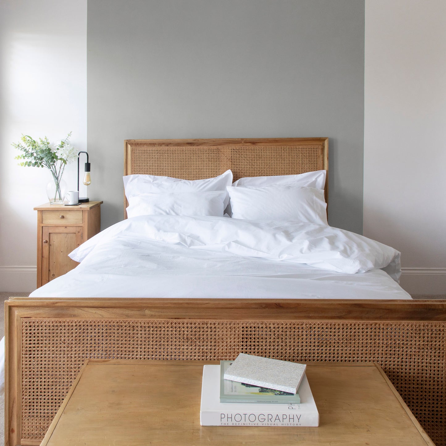 Bedroom with wooden bed frame, white 100% Pure Organic Cotton bedding, including duvet, pillow cases and fitted sheets, and a small table with books.