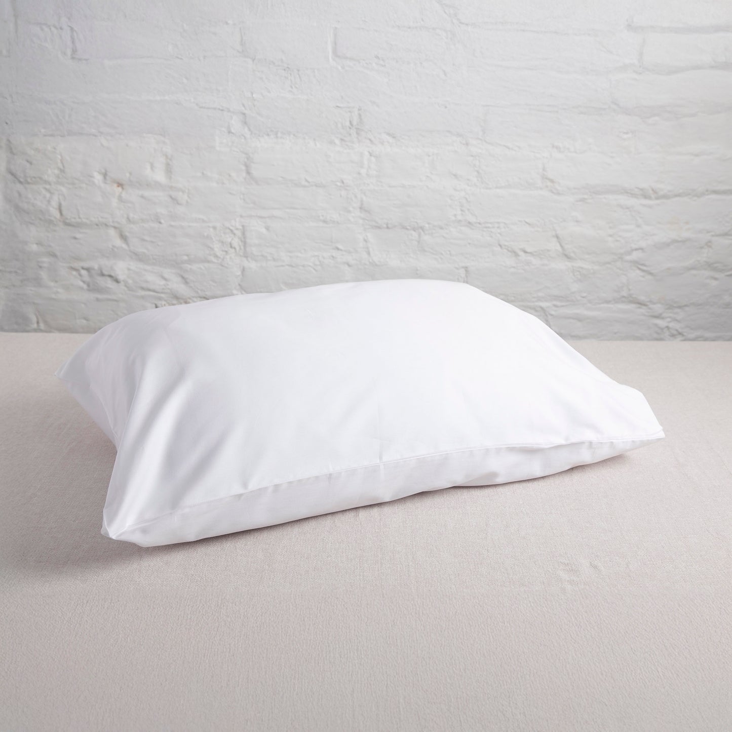 White sea salt 100% GOTS certified organic cotton pillow on a light gray bed against a white brick wall.