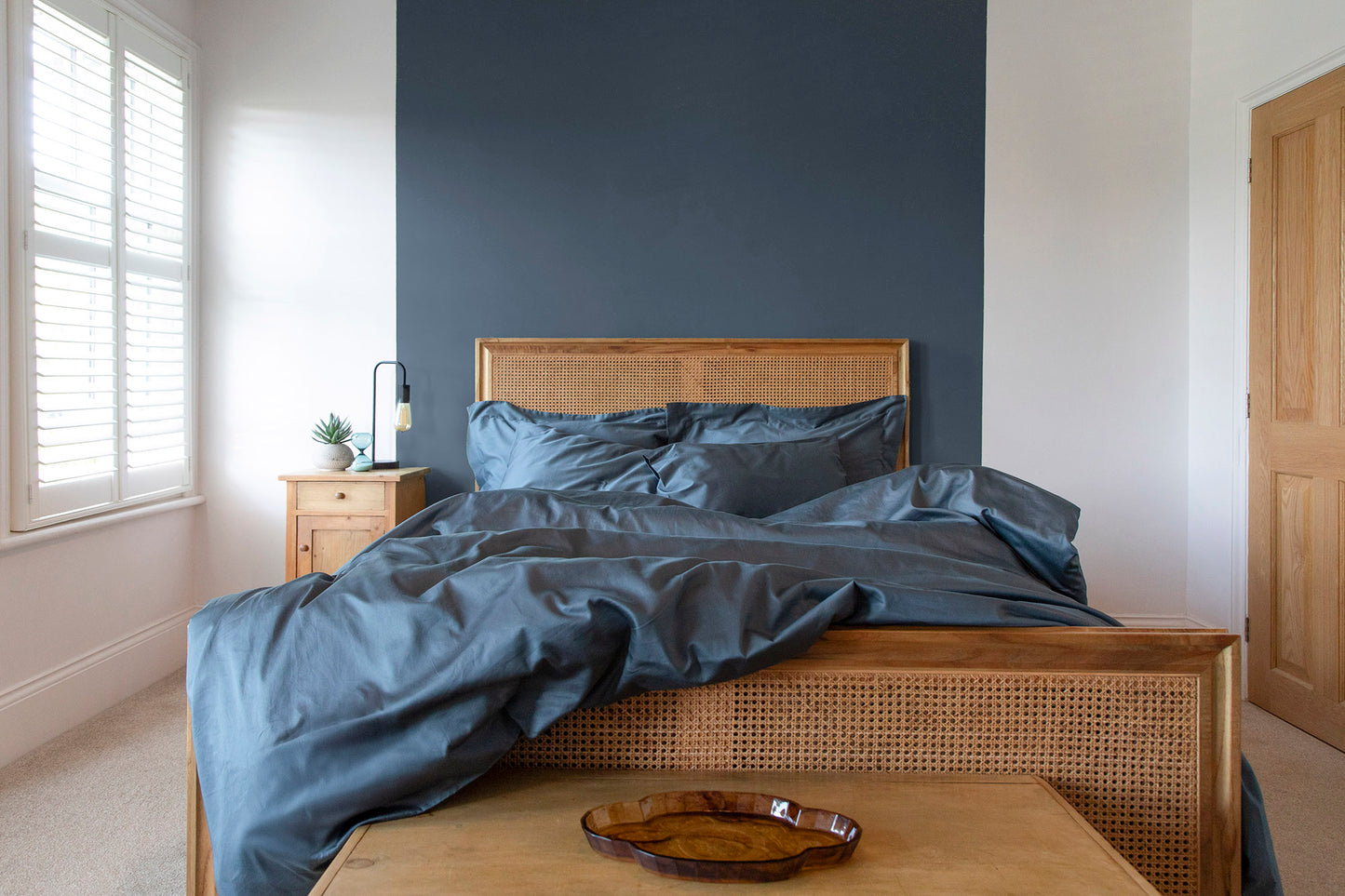 Bedroom with a bed featuring sargasso blue 100% cotton GOTS certified sateen bedding and a wooden headboard against a dark wall.