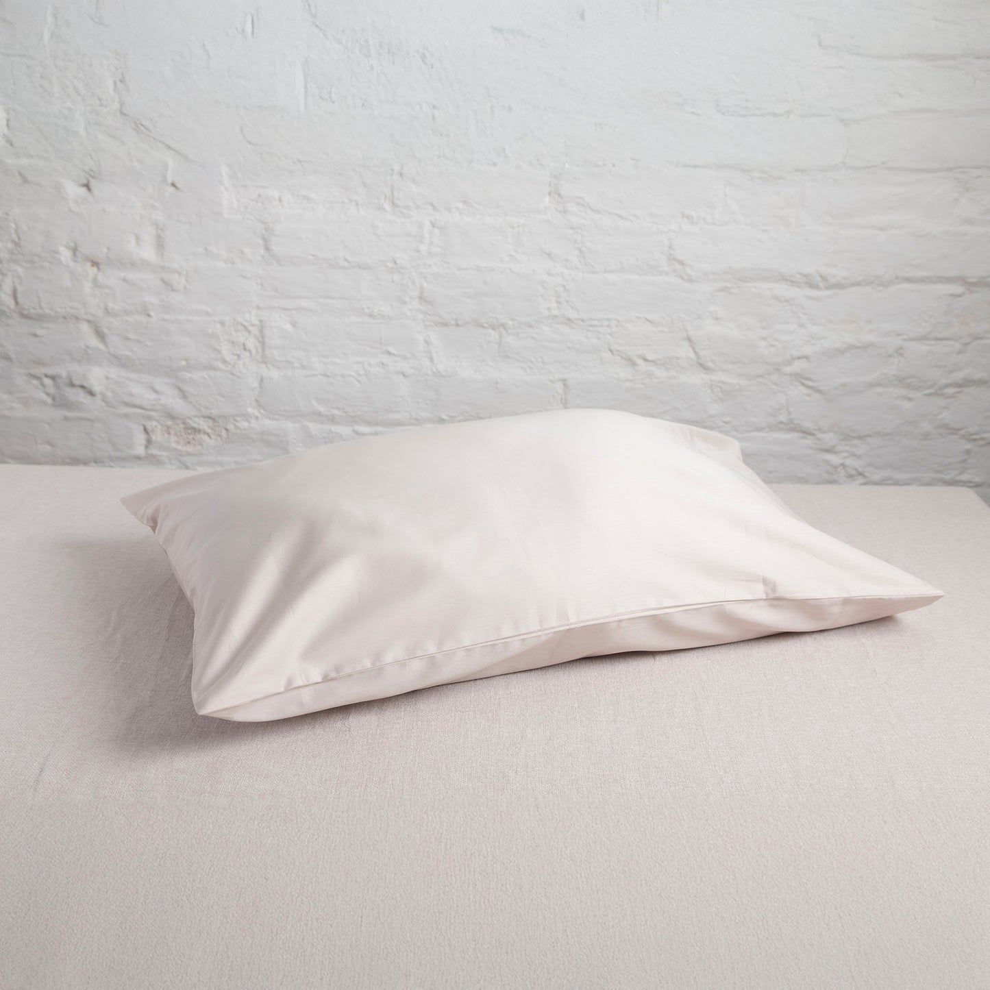 White pillow on a light gray surface with a white brick wall background – Linen Bay UK
