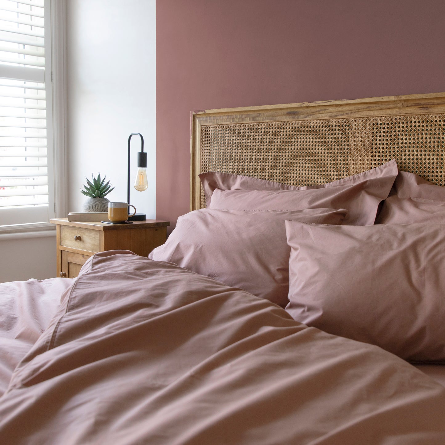 Neatly made bed with light pink bedding and a wooden headboard in a bedroom – Linen Bay UK