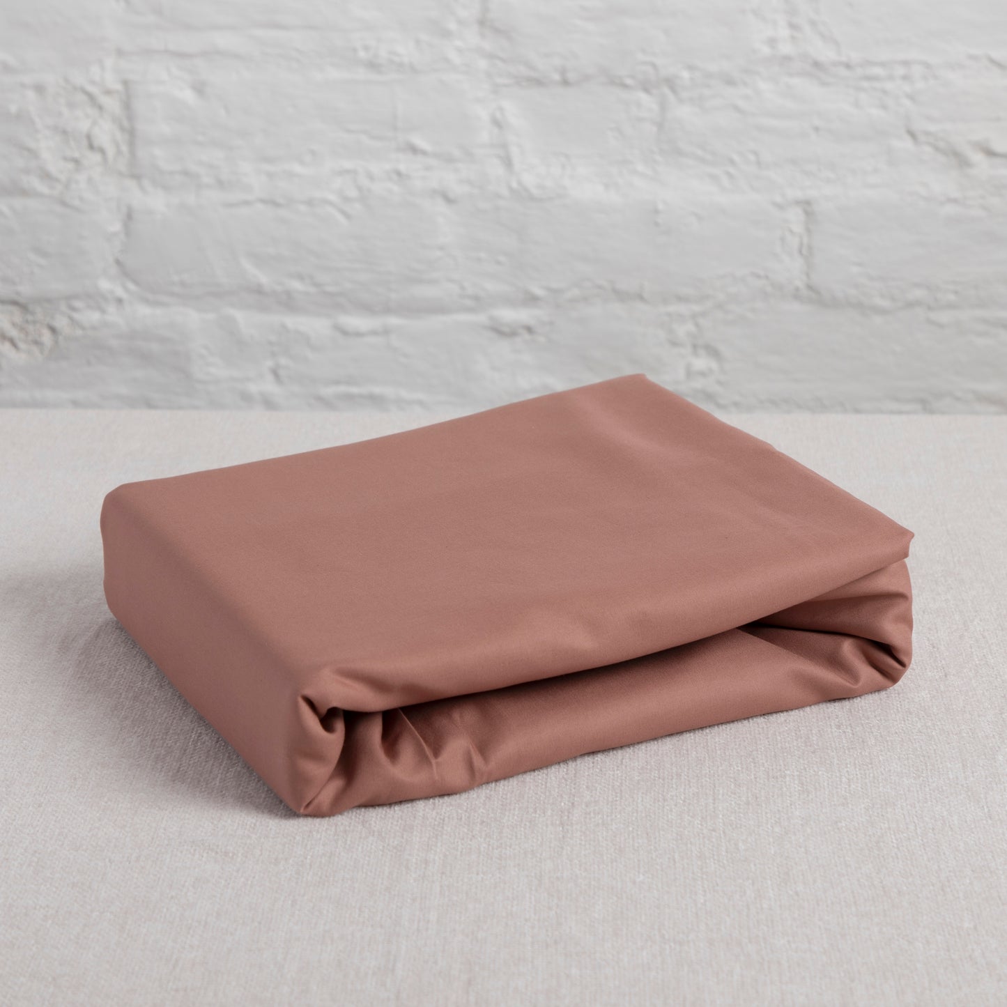 Folded dune shadow cotton flat sheet on a light gray surface with a textured gray wall background – Linen Bay UK
