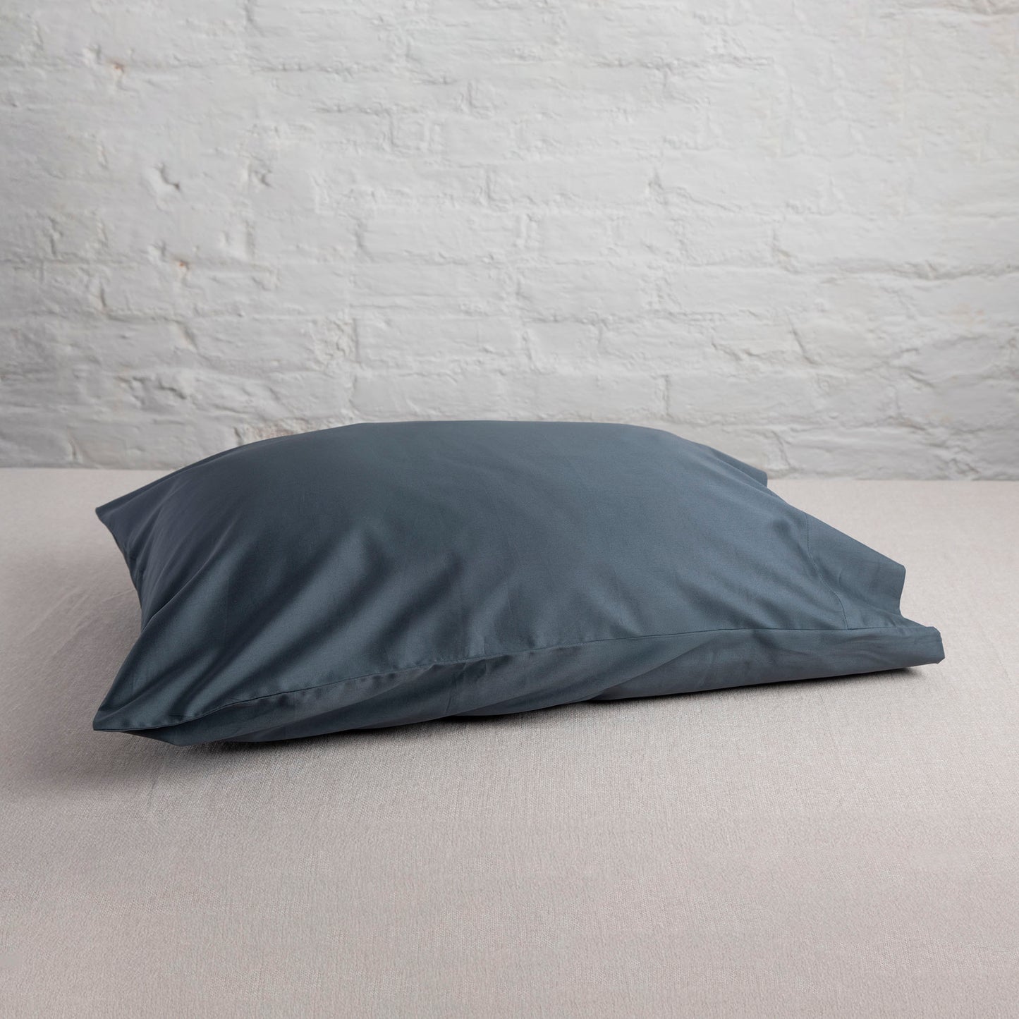 Sargasso Blue coloured pillow on a neutral fabric with a light gray wall background – Linen Bay UK