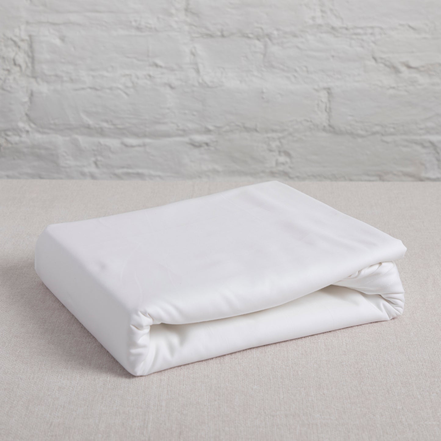 Folded white flat sheet on a light gray surface with a textured gray wall background