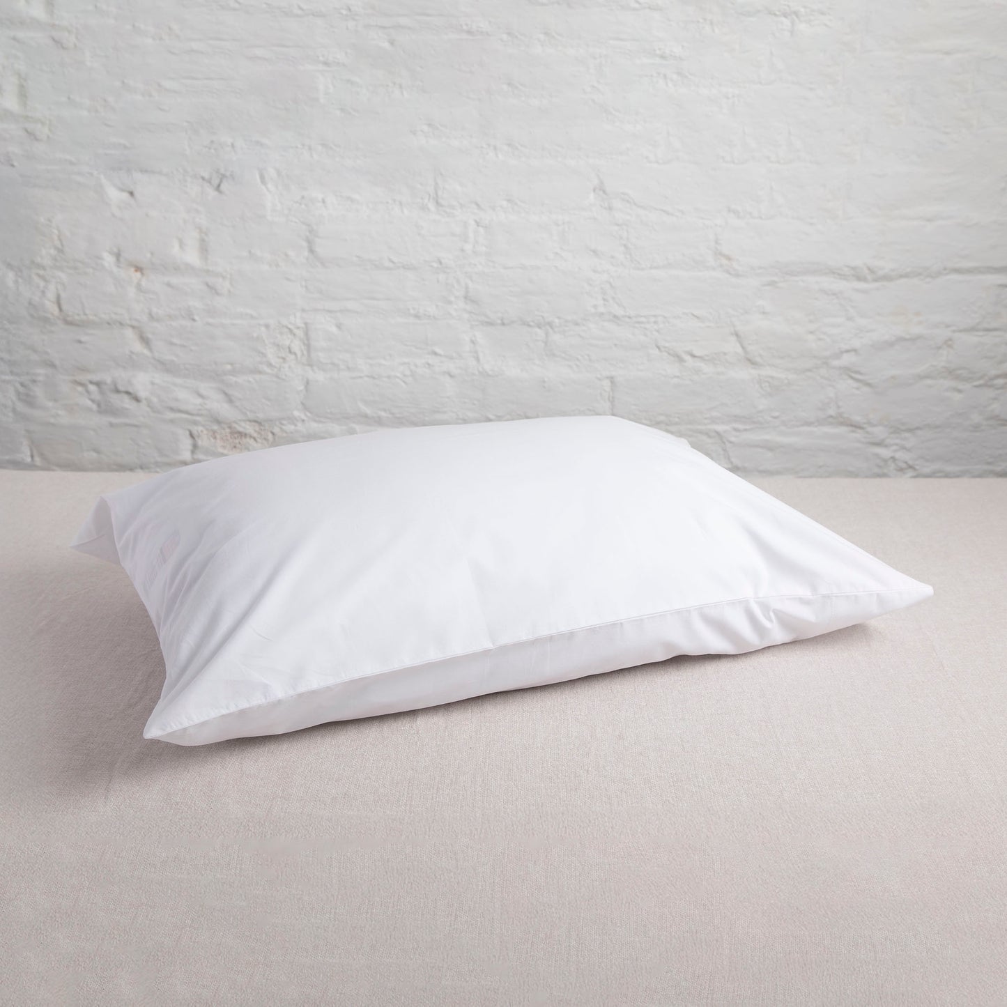 White pillow on a light gray surface with a light gray brick wall background