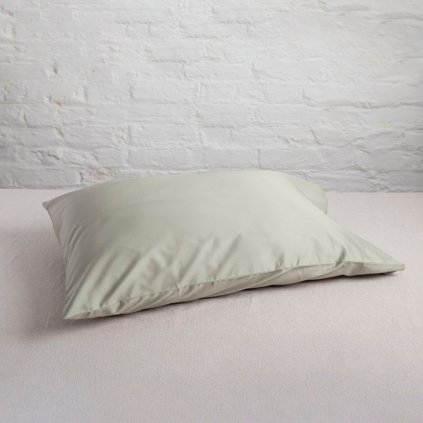 seagrass coloured green pillow on a bed with a light gray wall background – Linen Bay UK