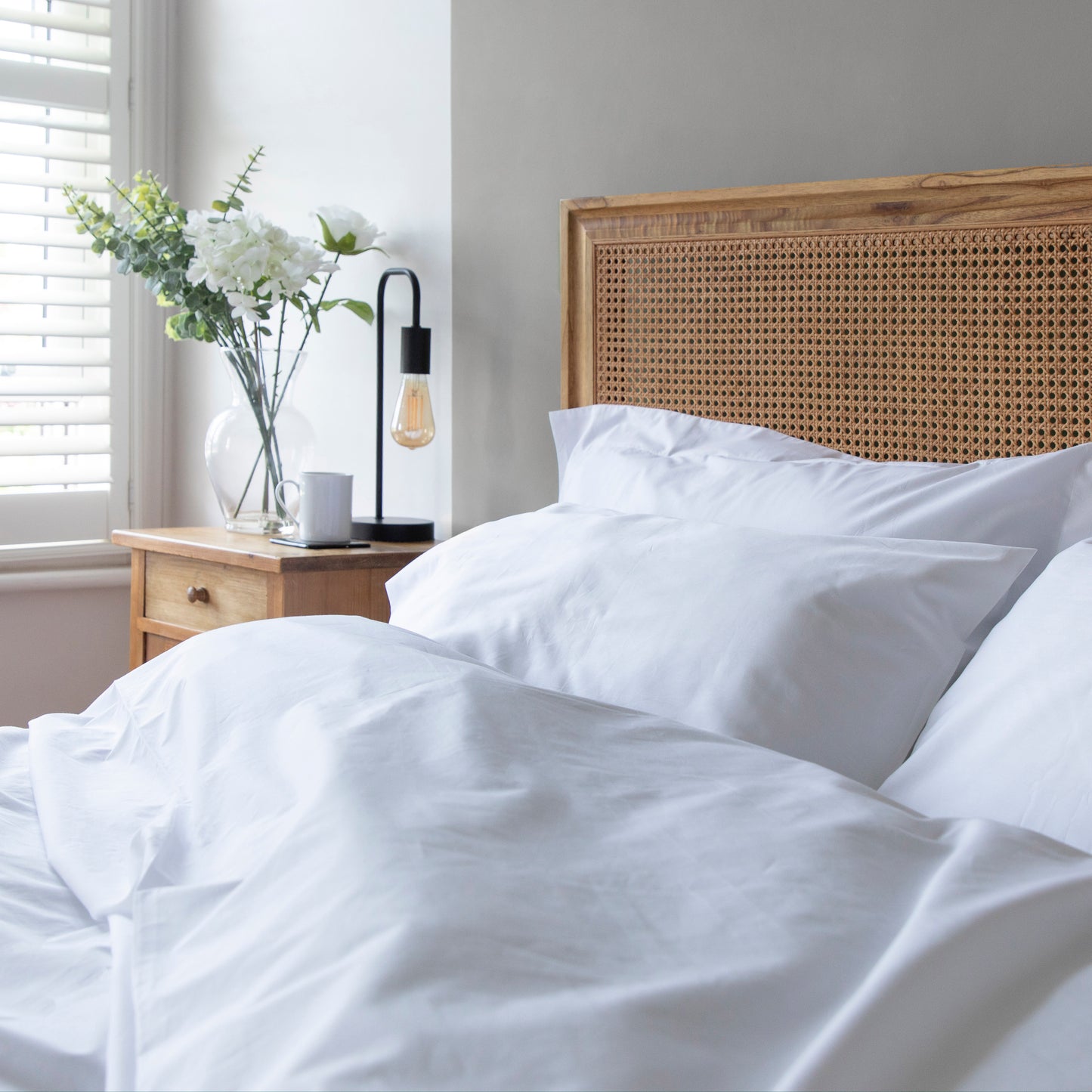 Bed with white bedding and a wooden headboard in a bright room.